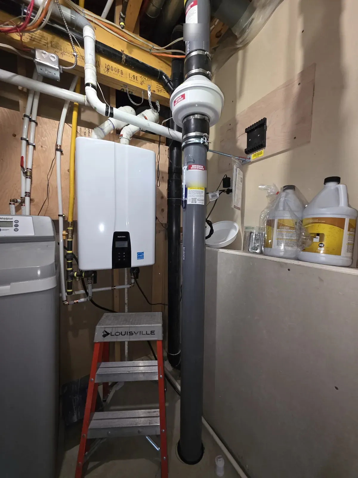 Radon mitigation system in a Calgary basement utility room, with an inline fan on grey vent pipe beside a tankless water heater