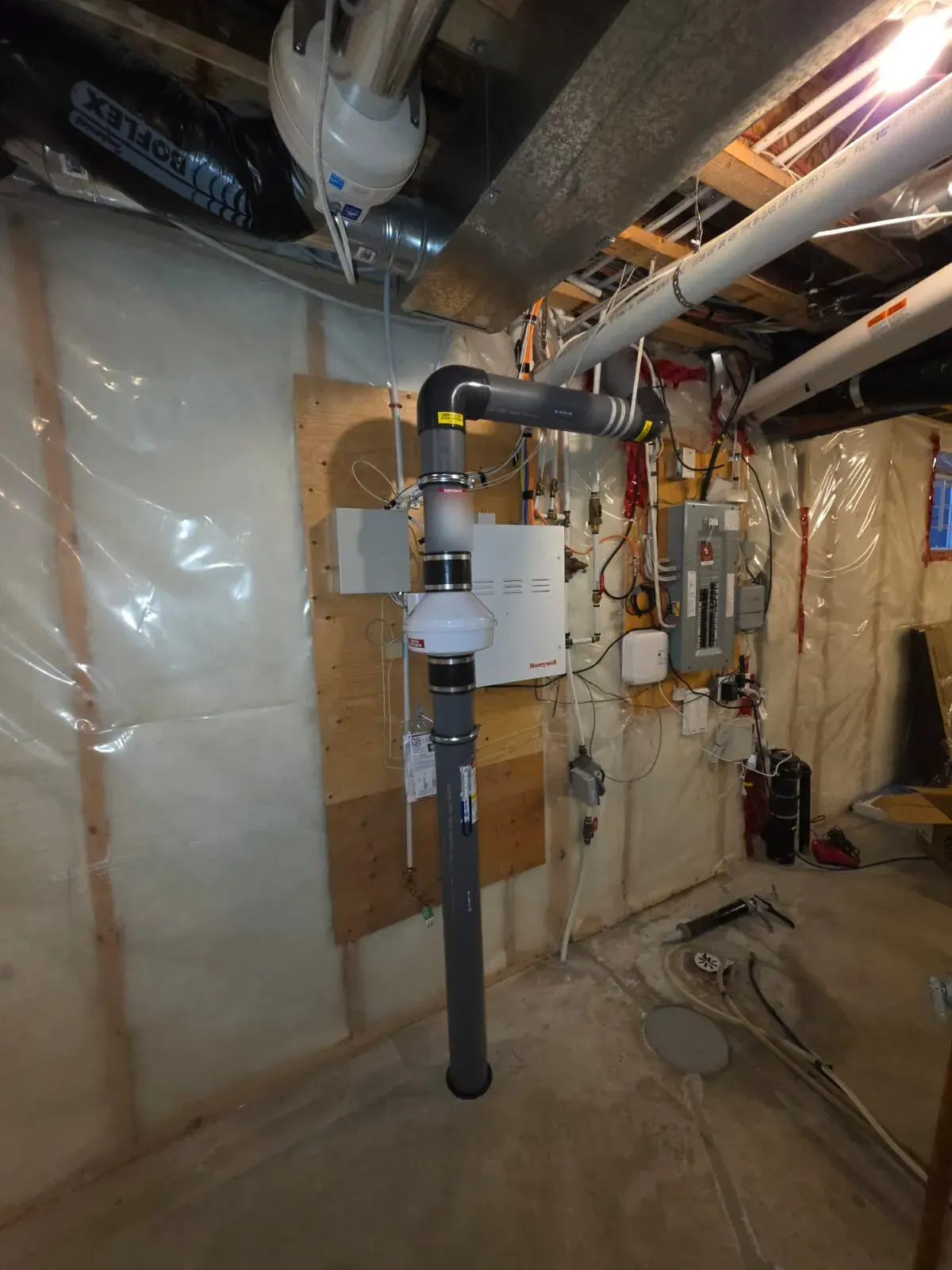 Sub-slab depressurization system in an unfinished basement: suction pipe through the slab, inline radon fan, and pipe routed toward the rim joist