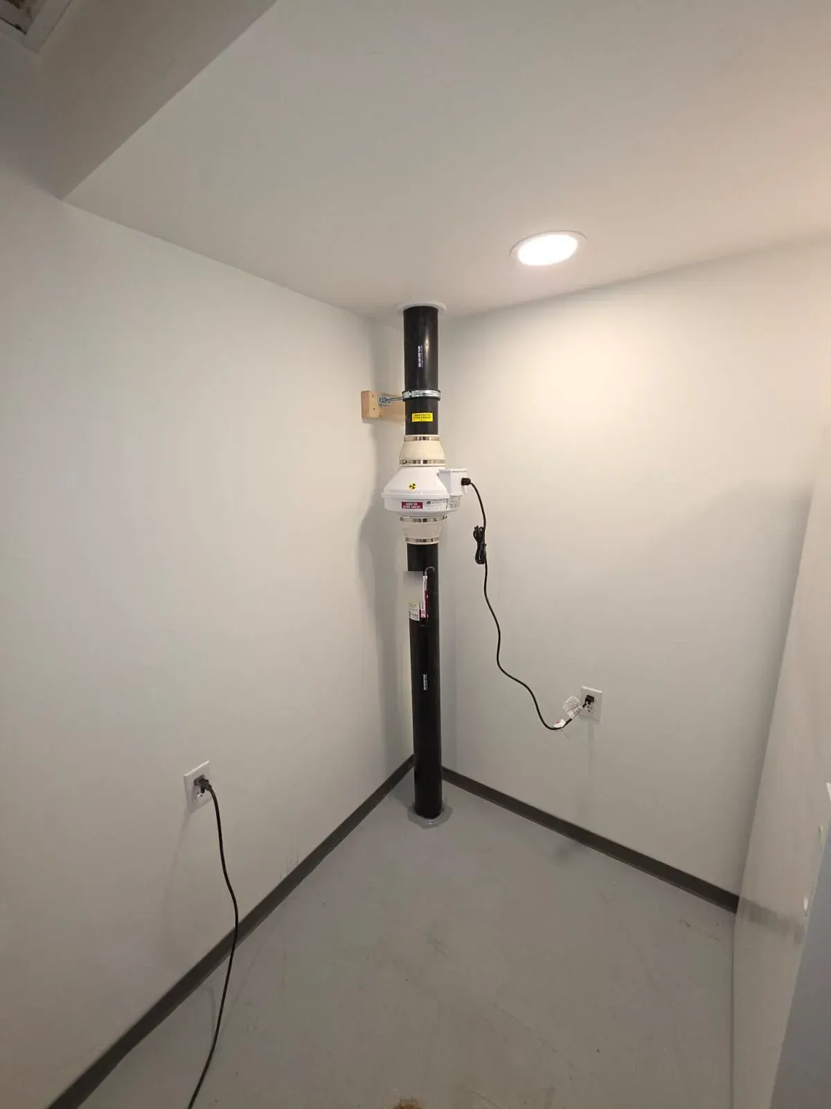 Radon vent pipe and fan neatly routed in the corner of a finished basement room
